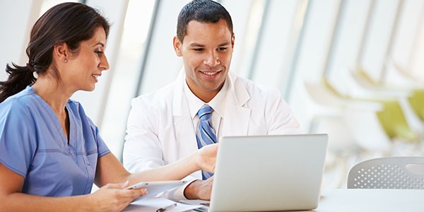 Two healthcare workers working on administrative work on a laptop