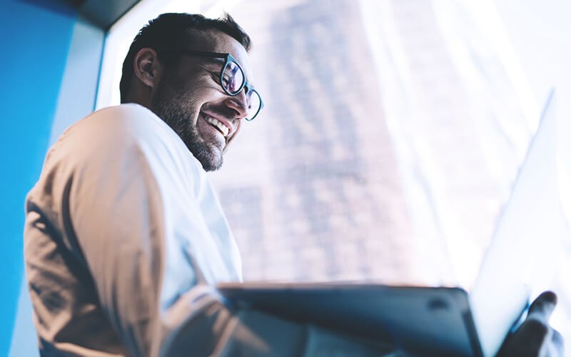 Office worker holding laptop smiling beside the window