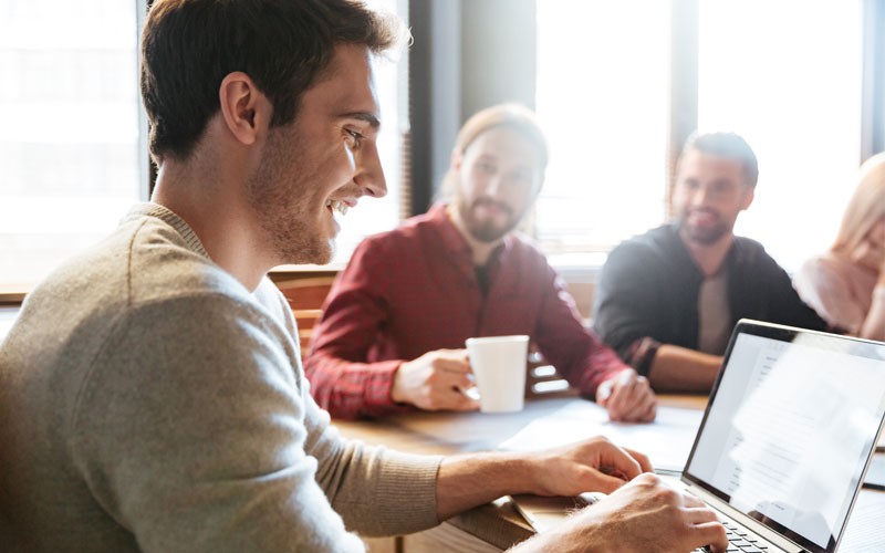 Man on laptop smiling as team enjoys success.