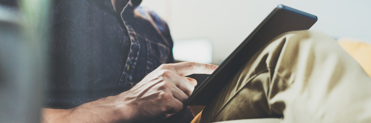 Bearded man sitting with legs crossed working on a tablet