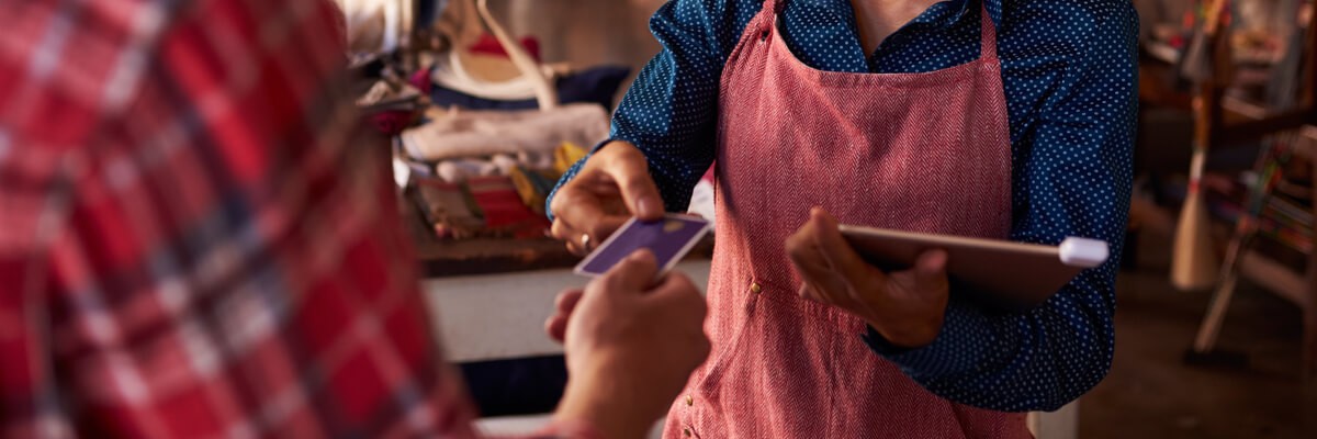 Shop owner taking a customer's payment using an iPad and cloud-based payment dongle. Retail technology. Customer experience.