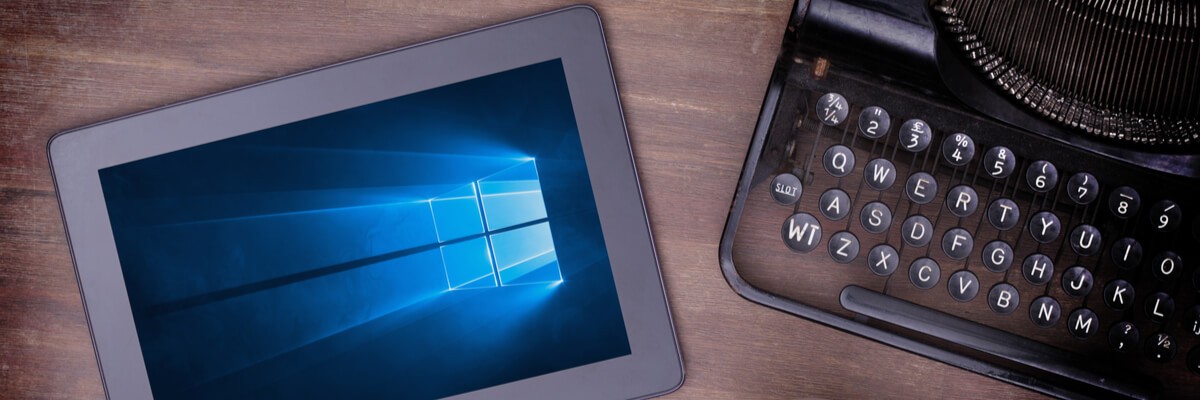 Tablet with Windows 10 in the background next to a typewriter, coffee and cookies.