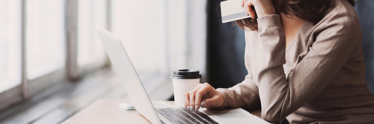 A woman sits on her laptop with a credit card in her hand.