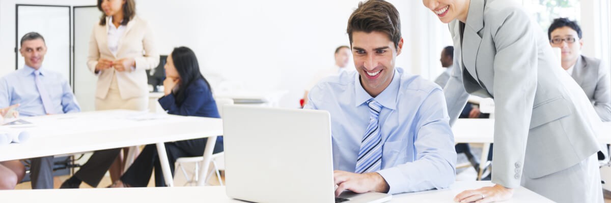 A business man and woman are looking at a computer, smiling.