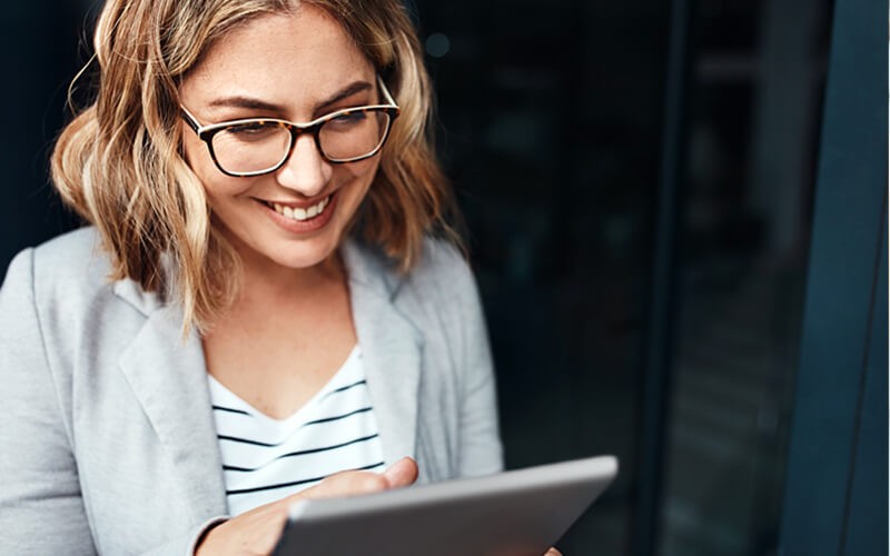 Smiling businesswoman on tablet device outside office