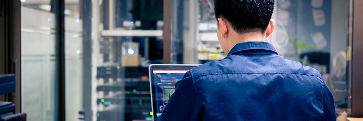 Server technician standing near data center while working off laptop computer