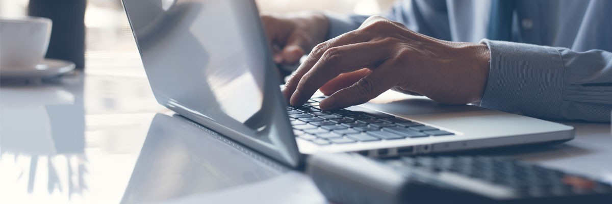 Business professional typing on laptop computer with calculator on desk