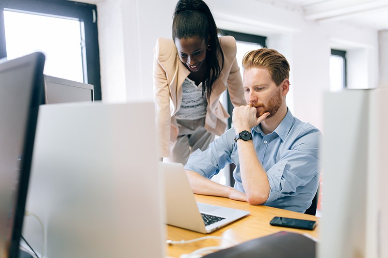 Business woman advising male colleague over desktop computer