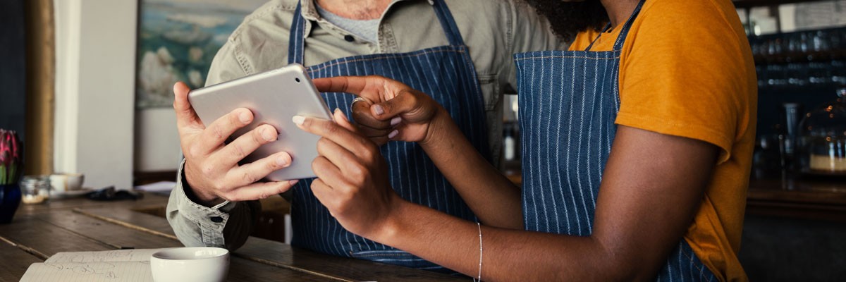 Two café owners and baristas view business information on tablet device