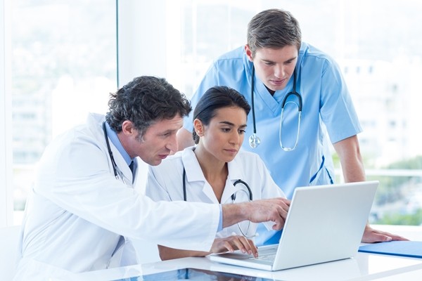 Three doctors in an office conferring at a desktop.