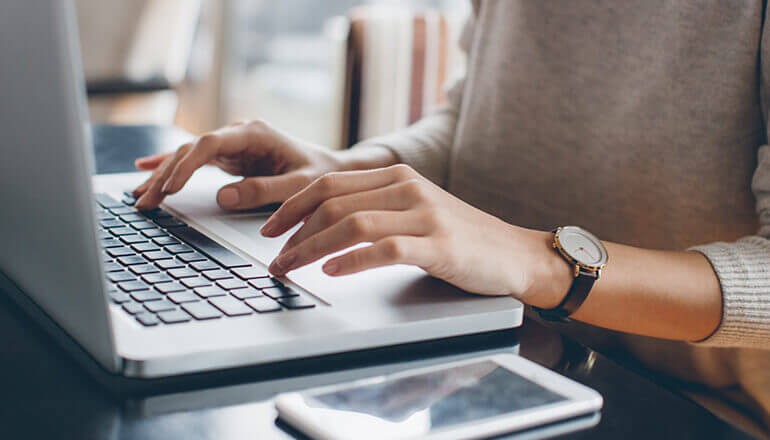 Close up of businesswoman using laptop device with phone on table