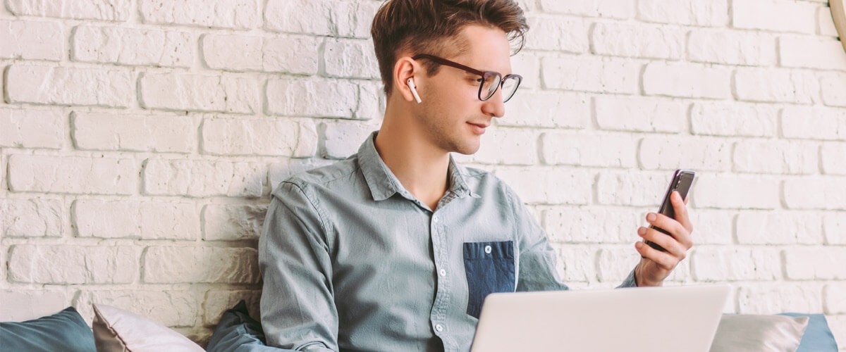 Man looking at cellphone while using a laptop