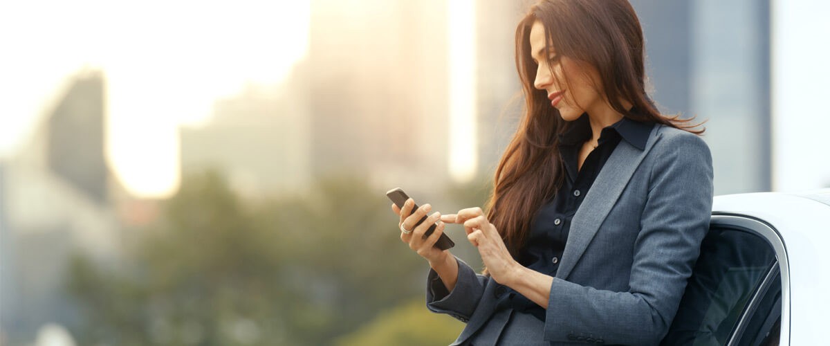 Business woman using cellphone leaned against car