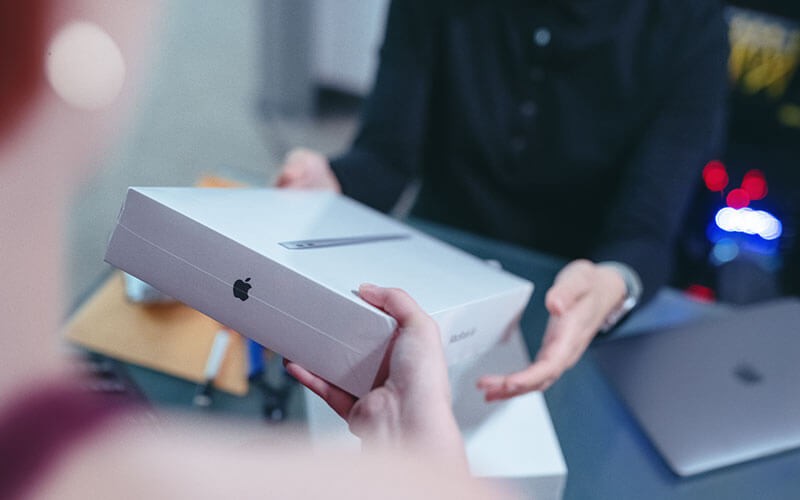 User handing new Mac in box to another user