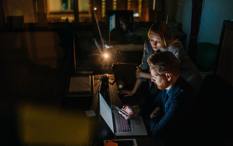 Two workers working on laptop in office late at night