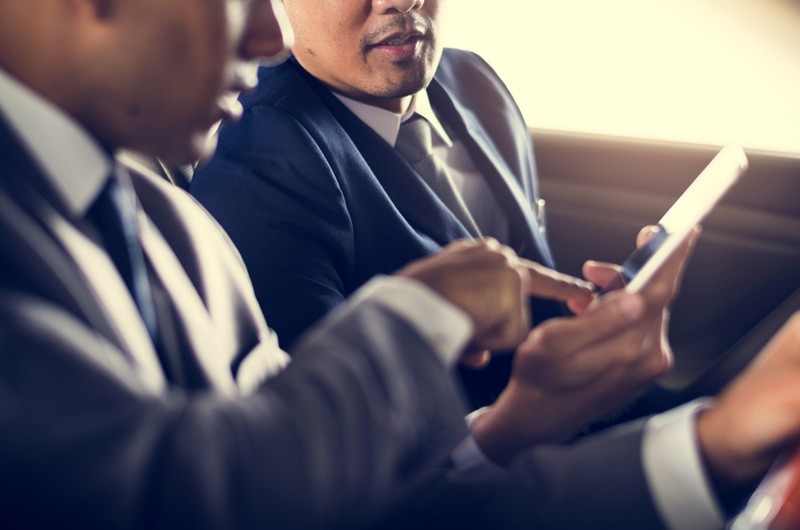 Two business men in a car looking at smart phone.