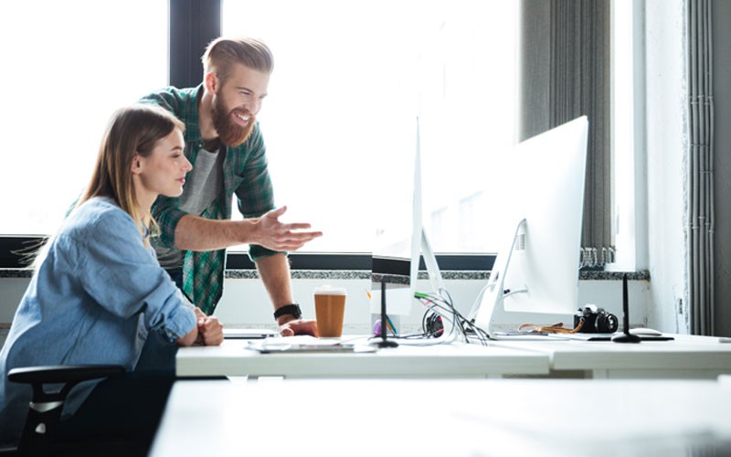 Two smiling business colleagues collaborate over desktop computer