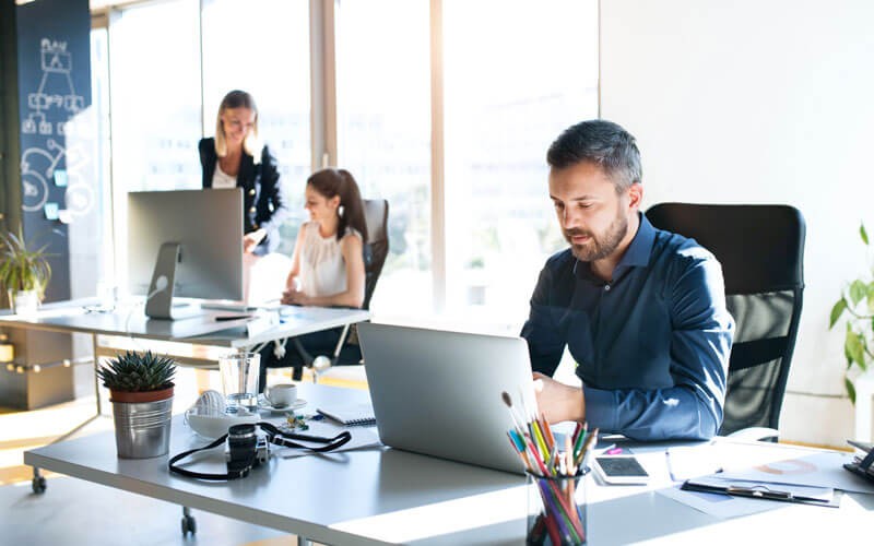 Businessman on laptop device with coworkers working in background