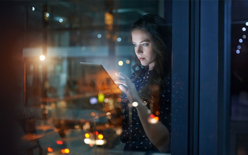 Woman working in office at night holding laptop device